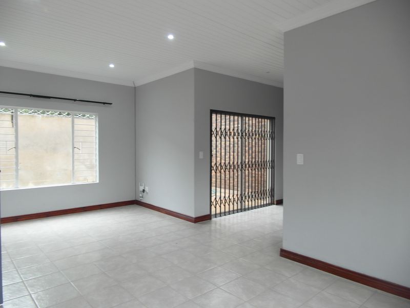 A bright, empty living area featuring neutral grey walls, tiled flooring, timber skirting, and a sliding door leading to an outdoor space.