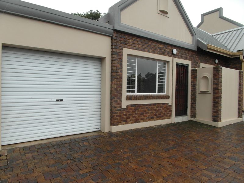Front elevation of a townhouse featuring a single roller garage door, brick facade, security gate, and a paved driveway.