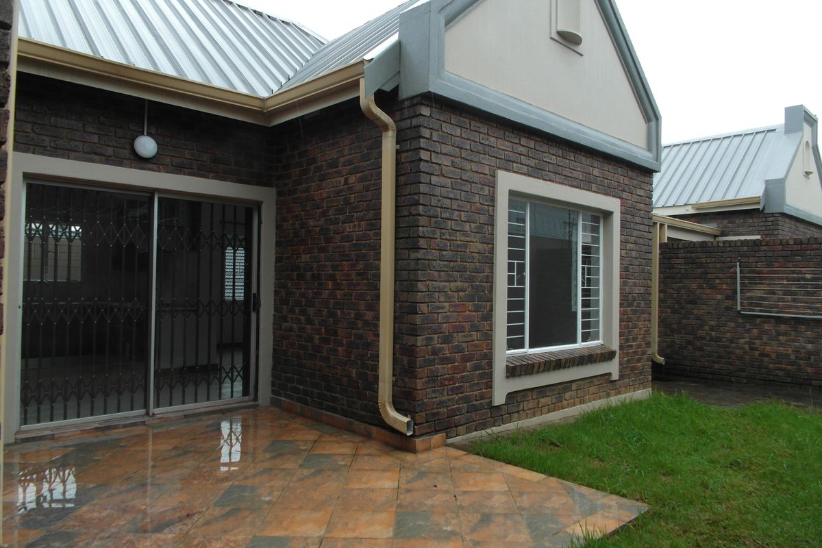 Rear view of the townhouse featuring a face brick facade, a tiled patio area, and secure sliding door access.