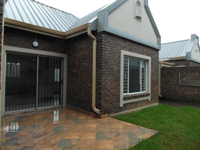 Rear view of the townhouse featuring a face brick facade, a tiled patio area, and secure sliding door access.