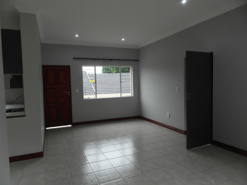 An empty open-plan living area featuring neutral grey walls, tiled flooring, recessed lighting, and a view through the window.
