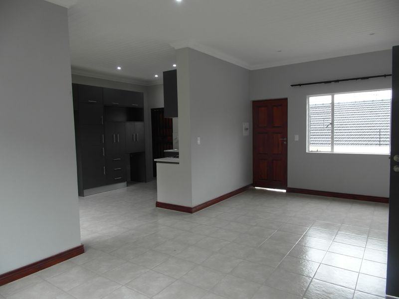An open-plan living and kitchen area featuring neutral grey walls, tiled flooring, recessed lighting, and dark built-in cabinetry.