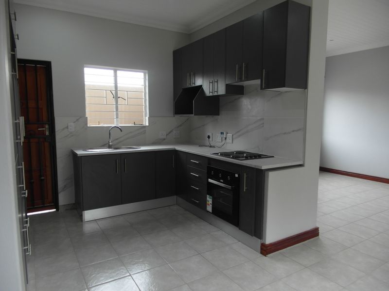 Modern kitchen featuring dark cabinetry, stone countertops, built-in oven and hob, and tiled flooring in an open-plan layout.