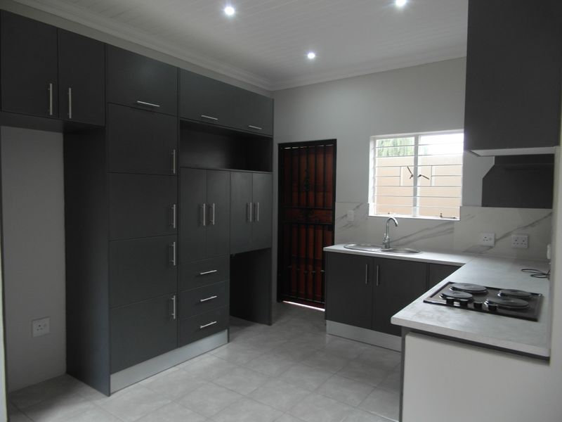 Modern kitchen featuring dark grey cabinetry, stone-look countertops, a built-in gas hob, and tiled flooring in a clean, well-lit space.
