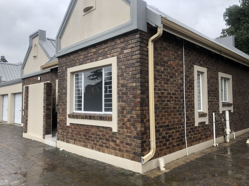 Exterior view of a face brick townhouse featuring a metal roof, security bars on windows, and a paved driveway leading to garage doors.