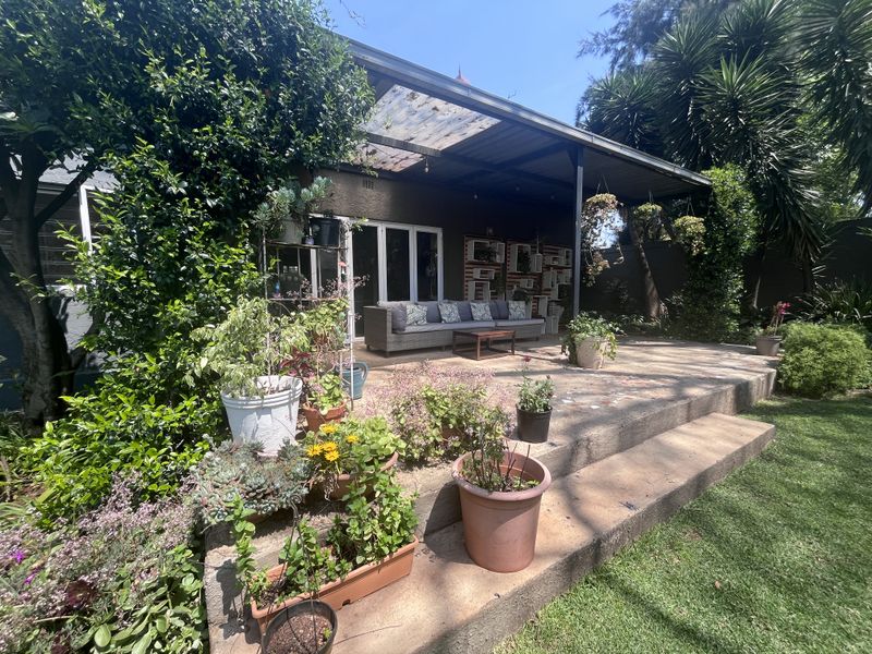 A covered outdoor patio area featuring concrete steps and sliding glass door access to the main house, set within a landscaped garden.