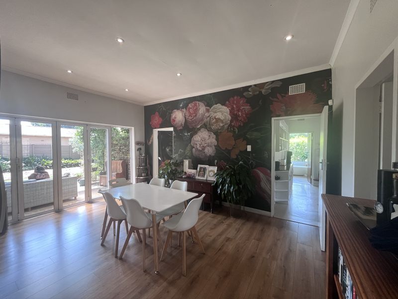 Spacious dining room featuring laminate flooring, recessed lighting, and large bi-fold doors opening to the garden, with a feature floral wall.