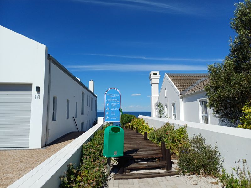 A view of a residential boardwalk path between two white houses leading towards the ocean in a coastal estate.