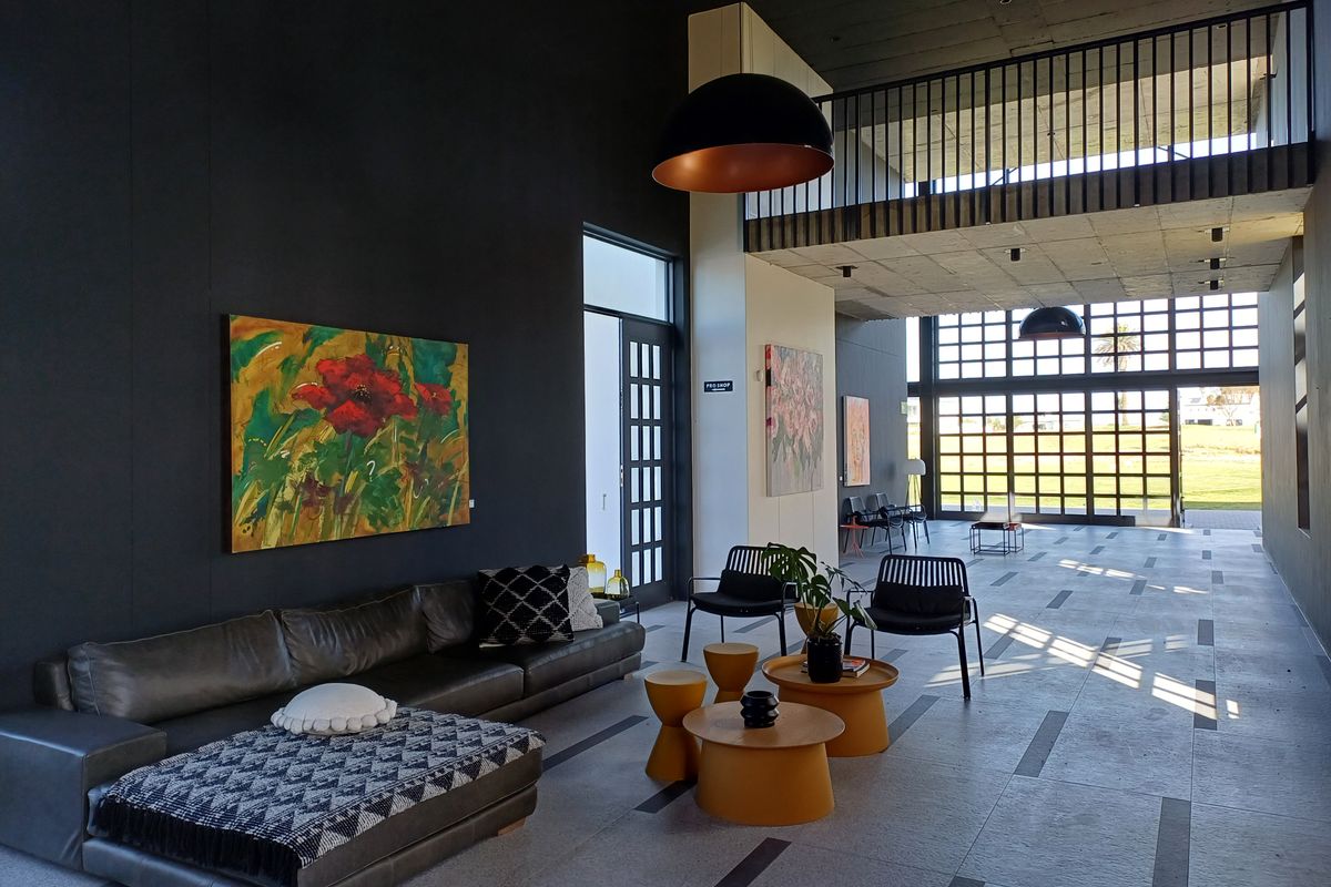 Spacious modern living area featuring high ceilings, exposed concrete elements, a mezzanine level, and large glass doors providing ample natural light.