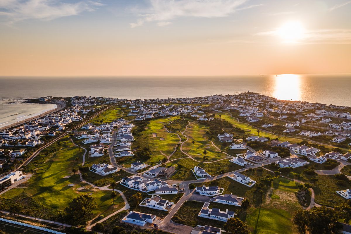 An aerial view of a coastal residential estate featuring a golf course, surrounded by ocean views at sunset.