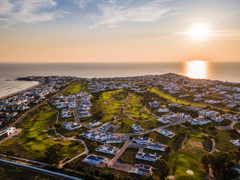An aerial view of a coastal residential estate featuring a golf course, surrounded by ocean views at sunset.