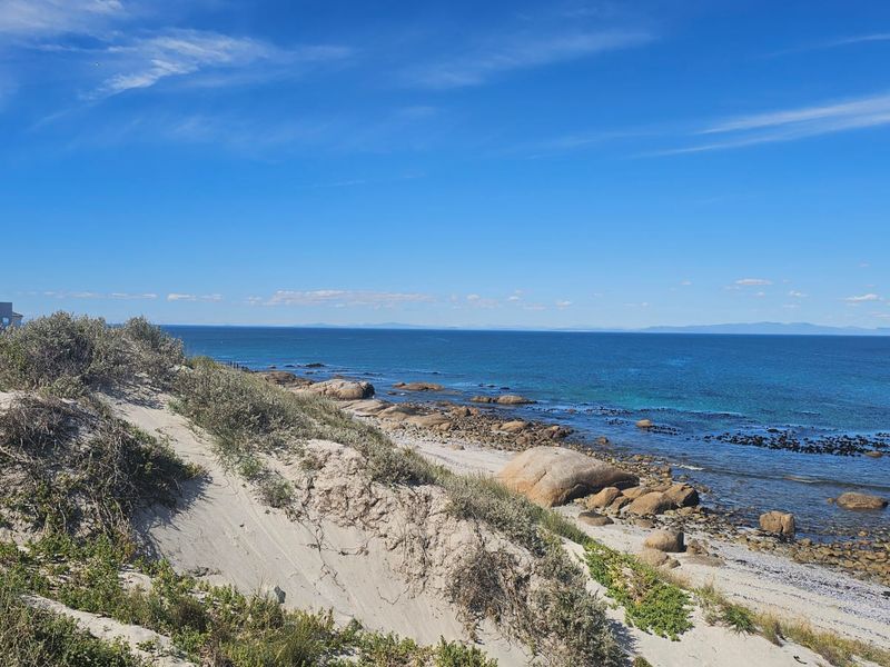 A scenic view of the coastline featuring natural sand dunes, rocky outcrops, and clear blue ocean waters adjacent to the residential property.