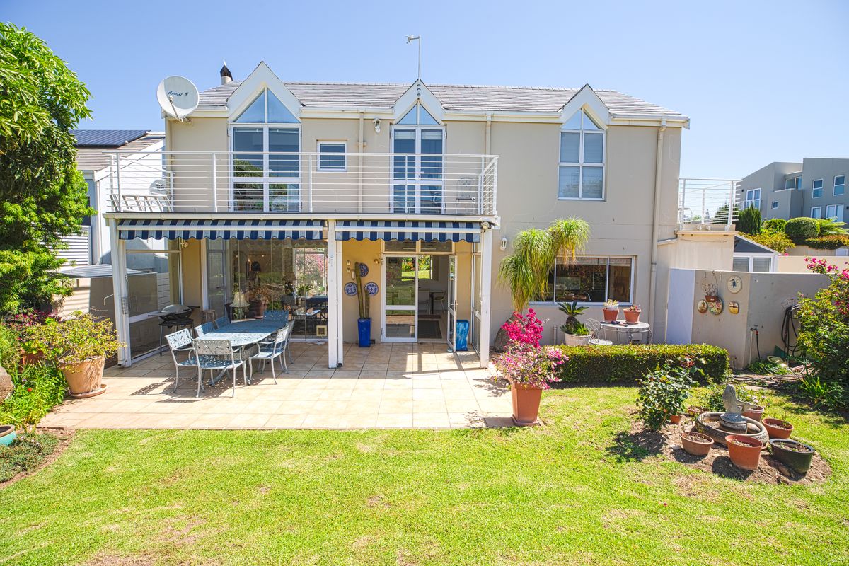 Rear view of a two-story house featuring a tiled patio, retractable awning, and an upper-level balcony overlooking a landscaped garden.