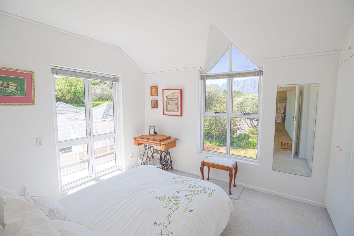 Bright bedroom featuring a vaulted ceiling, built-in wardrobe, full-length mirror, and large windows offering natural light and garden views.