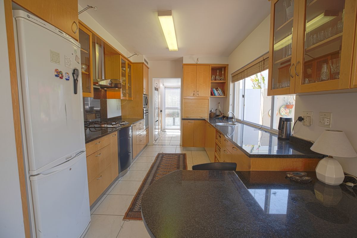 A functional kitchen featuring wooden cabinetry, granite countertops, built-in appliances, and tiled flooring, offering a practical layout with ample storage space.