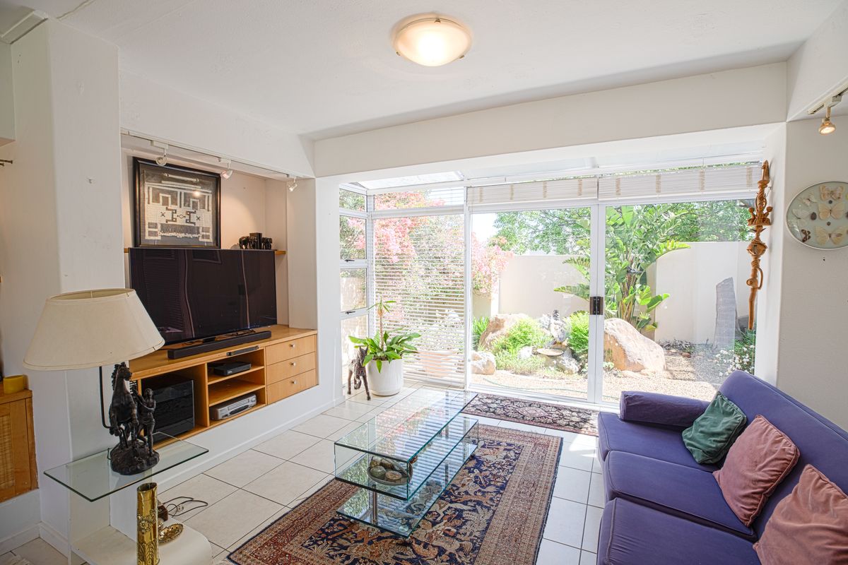 Bright living room featuring tiled floors, built-in cabinetry, and large sliding glass doors that open onto a private garden patio.