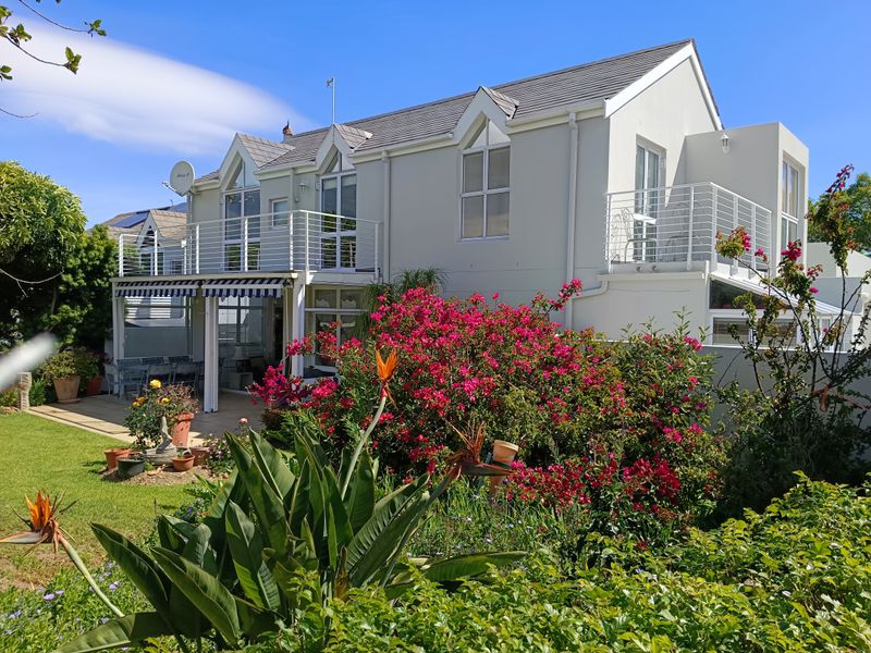 Rear view of a two-story house featuring a landscaped garden, a covered patio area, and upper-level balconies with metal railings.