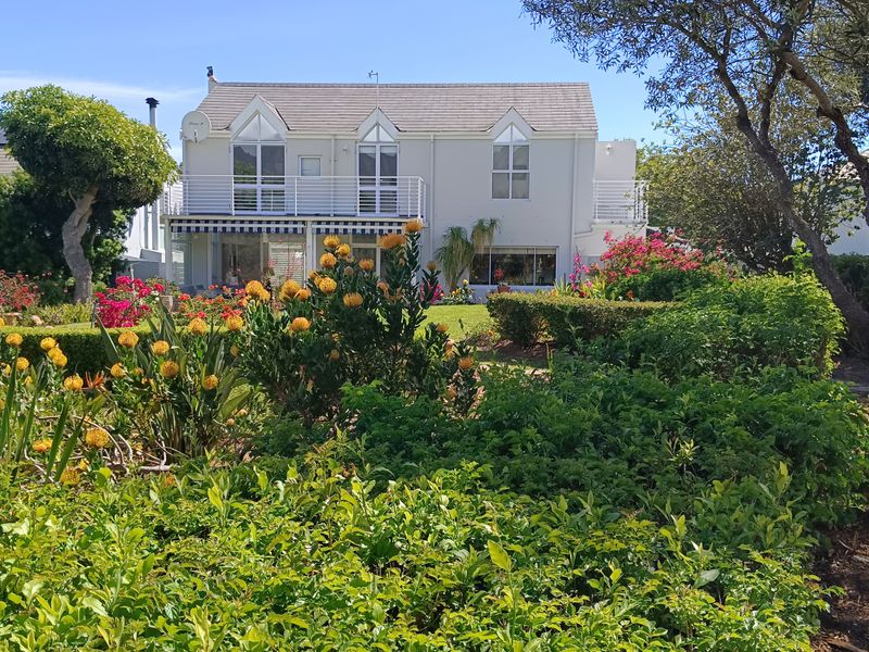 A well-maintained rear elevation of a two-story house featuring a balcony, retractable awning, and large glass doors overlooking a lush, landscaped garden.