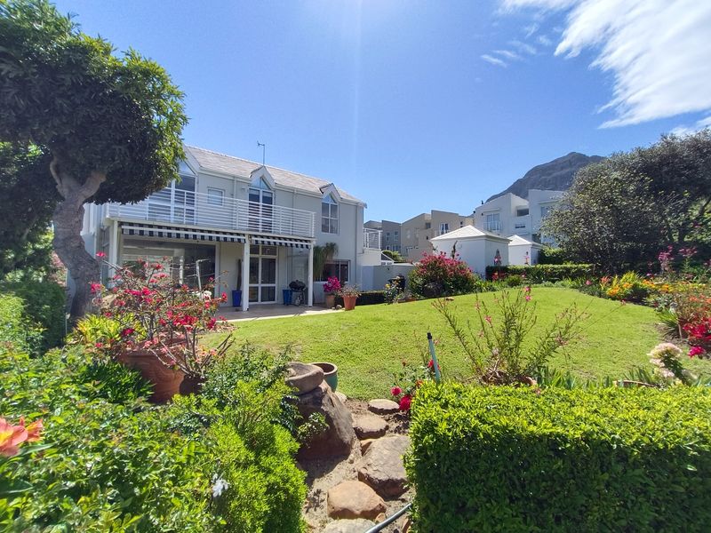 Rear view of the property featuring a well-maintained lawn, landscaped garden, and an upper-level balcony with a retractable awning.