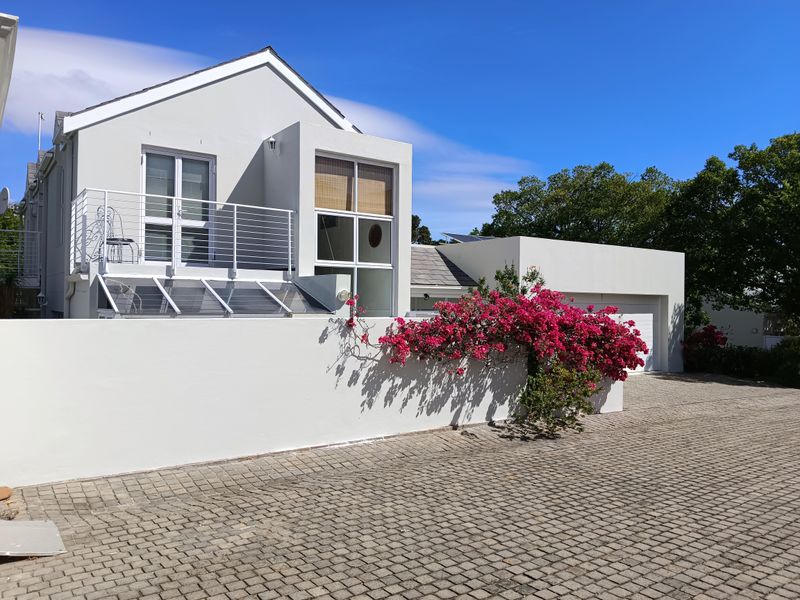 Front exterior view of a modern house featuring a paved driveway, boundary wall, balcony, and integrated garage.
