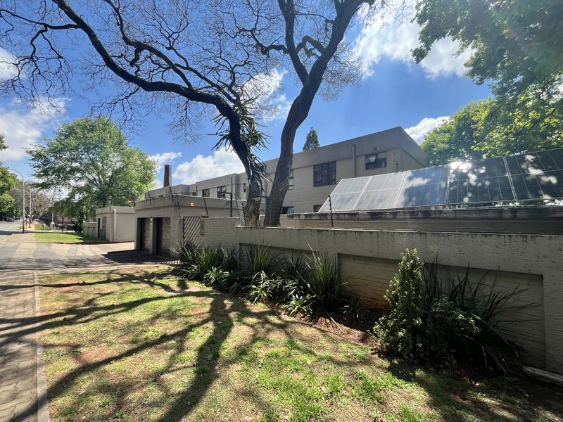 Front exterior view of the apartment complex featuring a brick boundary wall, integrated solar panels, electric fencing, and paved driveway access.