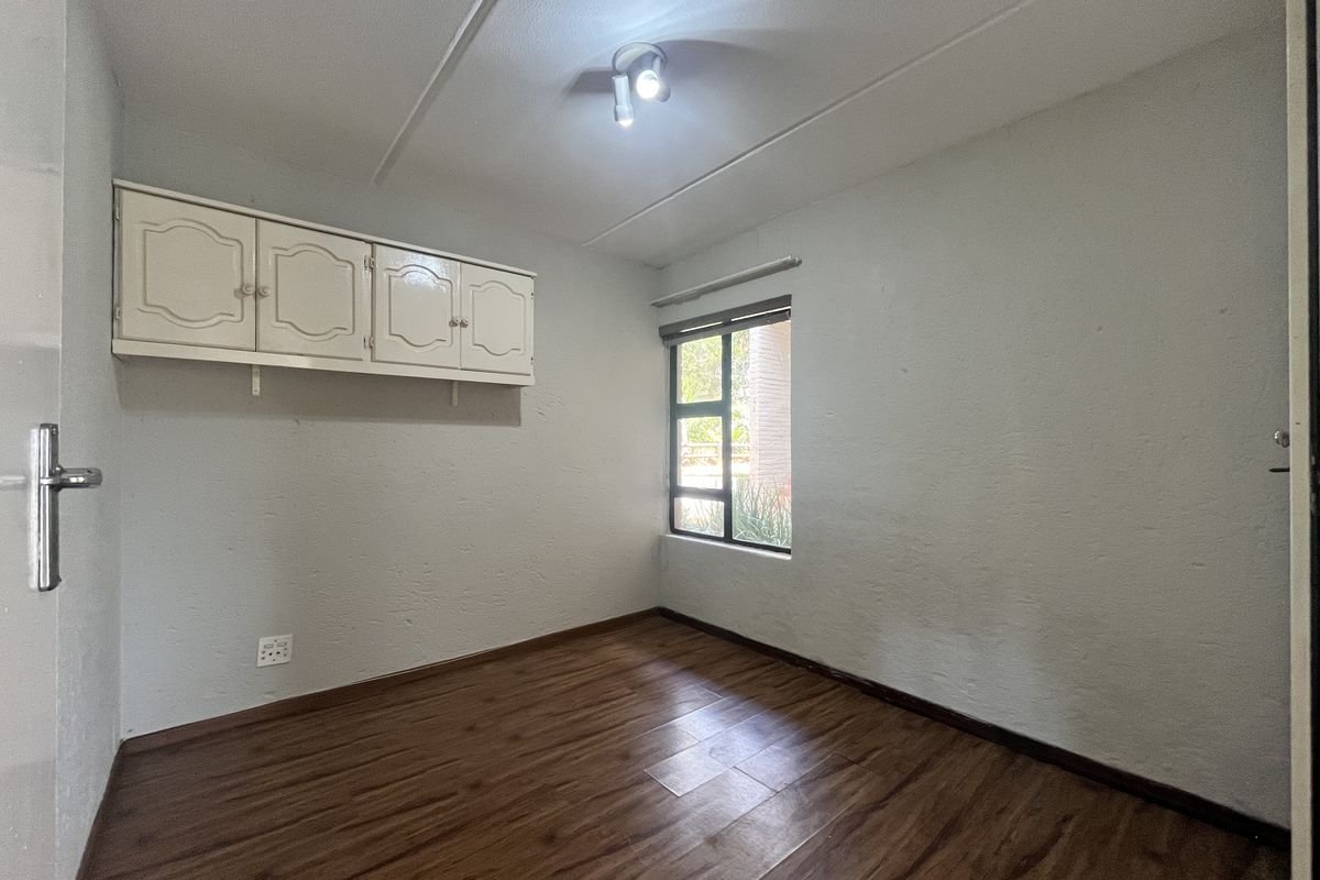 An empty bedroom featuring laminate flooring, built-in wall-mounted cabinetry, and a window with an aluminium frame.