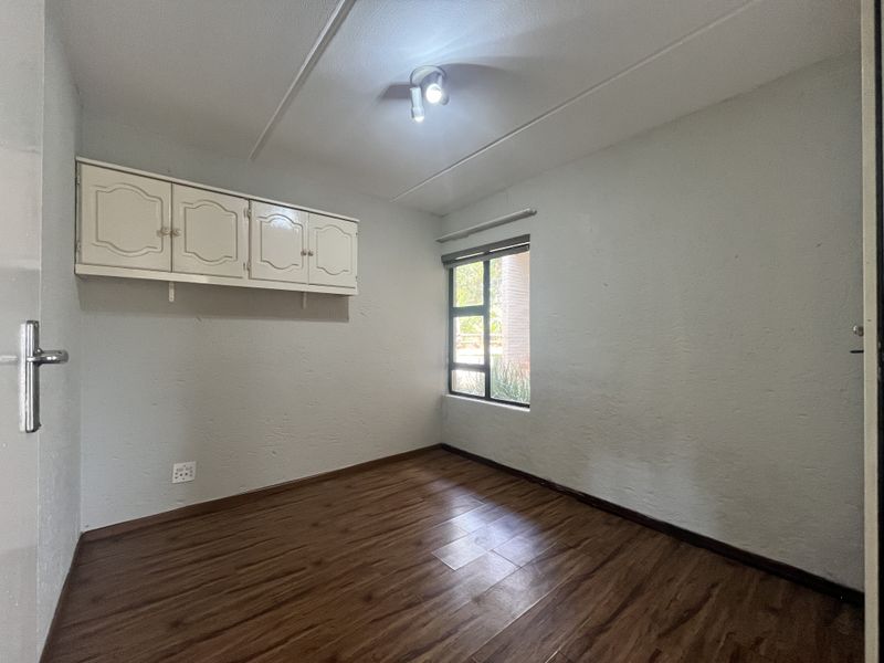 An empty bedroom featuring laminate flooring, built-in wall-mounted cabinetry, and a window with an aluminium frame.