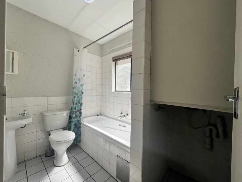 A functional bathroom featuring a pedestal basin, toilet, and bathtub with tiled finishes, requiring some cosmetic updates and plumbing concealment.