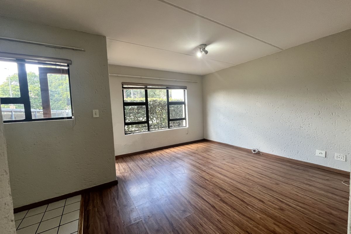 An empty living room featuring laminate flooring, textured walls, and aluminium-framed windows, offering a blank canvas for interior design.