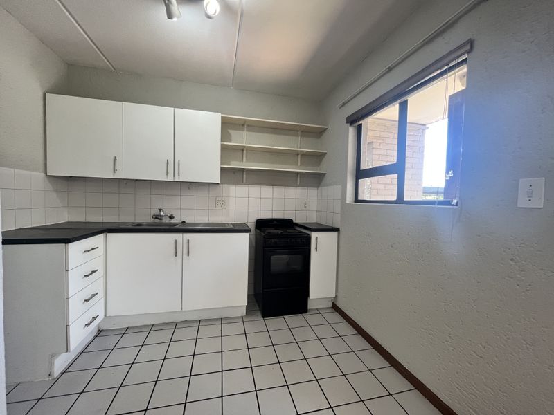A functional kitchen featuring white cabinetry, tiled backsplash, open shelving, and a freestanding stove, offering a clean and practical layout.