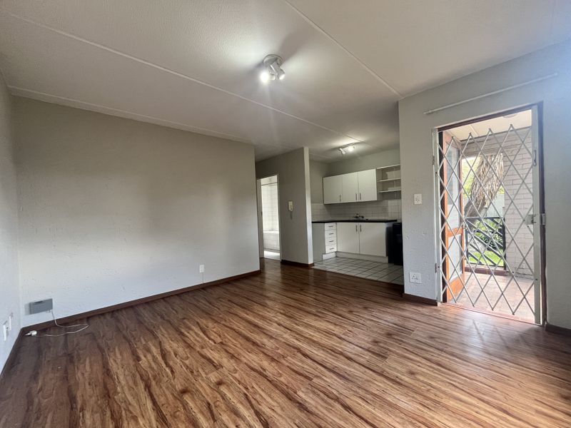 An open-plan living area featuring laminate flooring, a compact kitchen with built-in cabinetry, and a secure entrance door leading to an outdoor space.