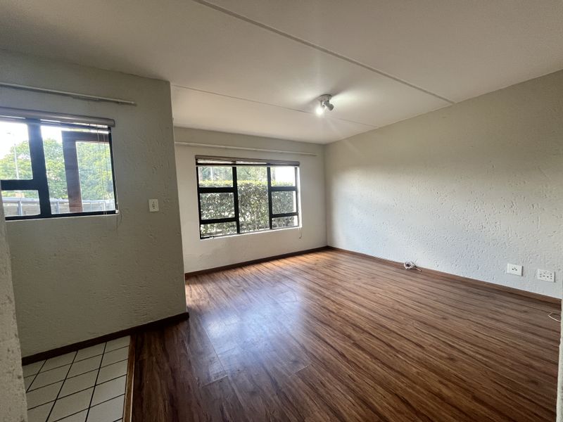 An empty living room featuring laminate flooring, textured walls, and aluminium-framed windows, offering a blank canvas for interior design.