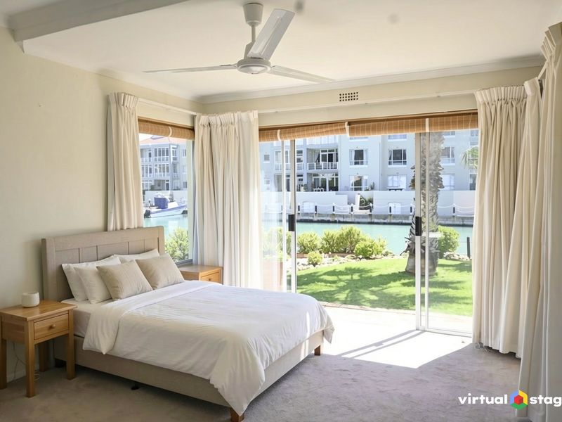A bright bedroom featuring a ceiling fan and large sliding glass doors that open to a scenic waterfront view.