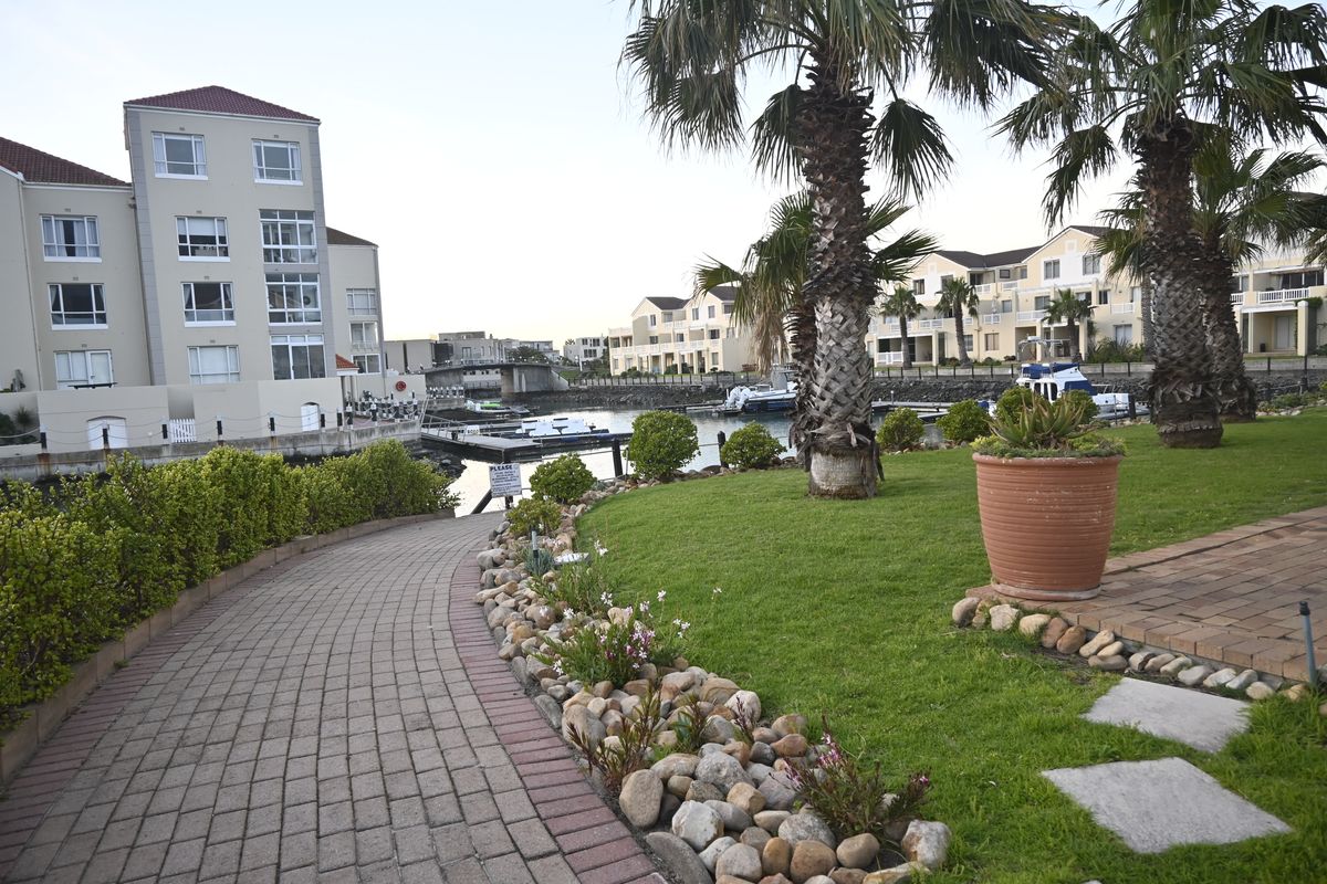 A well-maintained waterfront garden area featuring a paved walkway, landscaped lawn, and direct access to the canal with boat moorings.