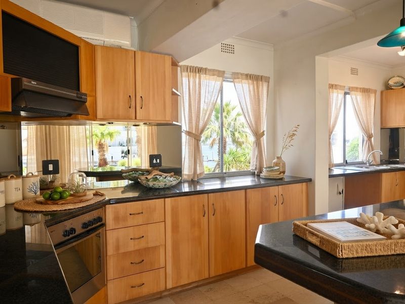 A well-maintained kitchen featuring warm wooden cabinetry, dark granite countertops, a mirrored backsplash, and a functional layout with an adjoining scullery area.