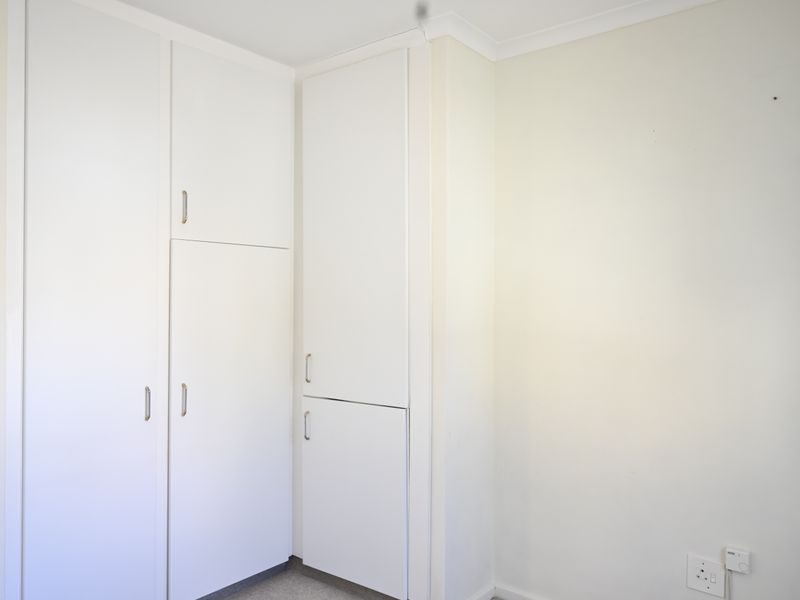 A clean, empty bedroom corner featuring white built-in cupboards and neutral wall finishes, providing a versatile space ready for personalization.