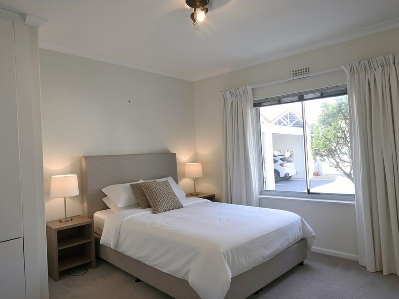 A well-maintained bedroom featuring neutral walls, carpeted flooring, a built-in wardrobe, and a window providing natural light and views of the exterior.