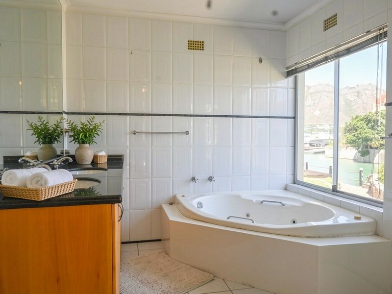 A bright bathroom featuring a corner bathtub, granite-topped vanity, and large window with scenic water views.