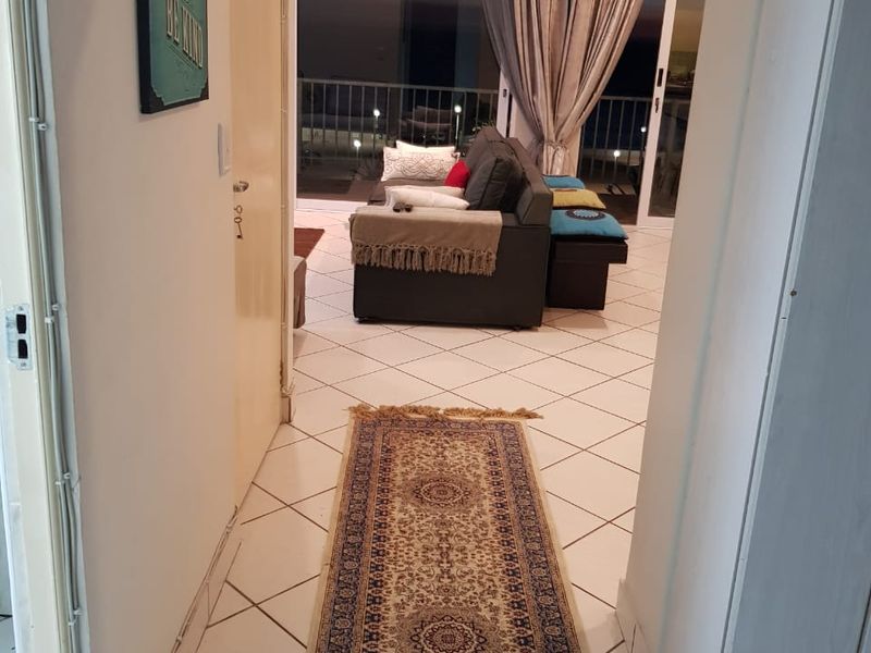 A tiled hallway leading into an open-plan living area with large sliding glass doors providing access to a balcony.