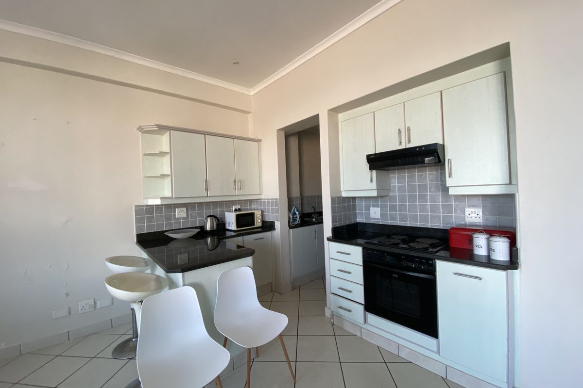 Functional kitchen featuring light-toned cabinetry, granite countertops, built-in oven, hob, extractor fan, and tiled flooring with an adjacent breakfast bar area.