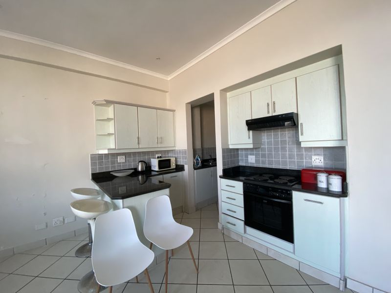 Functional kitchen featuring light-toned cabinetry, granite countertops, built-in oven, hob, extractor fan, and tiled flooring with an adjacent breakfast bar area.