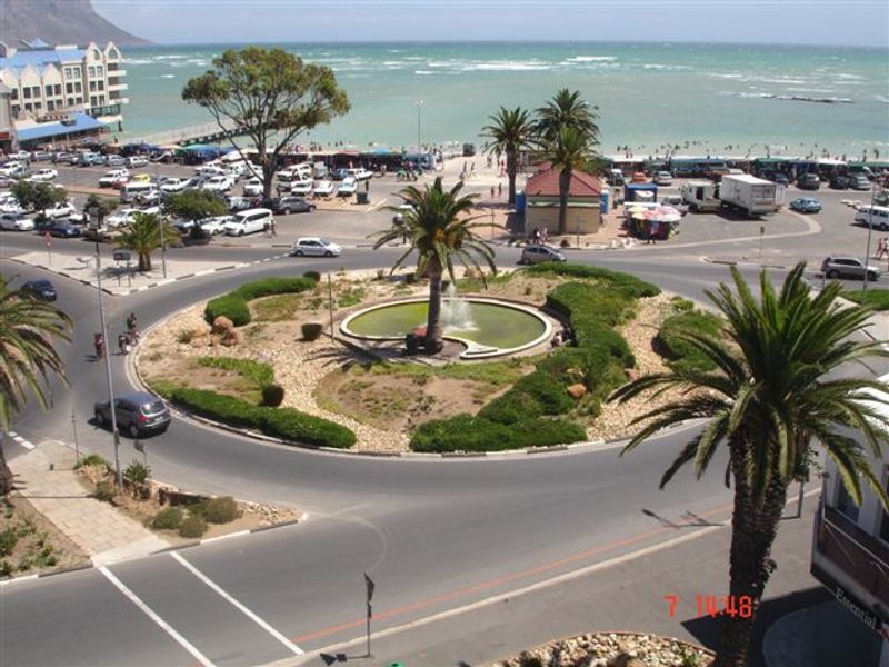 Elevated view overlooking a coastal roundabout, landscaped central fountain, and surrounding beach area.