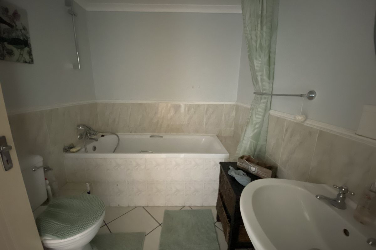 A functional bathroom featuring a bathtub with shower mixer, pedestal basin, and tiled finishes, offering a standard layout for an apartment.
