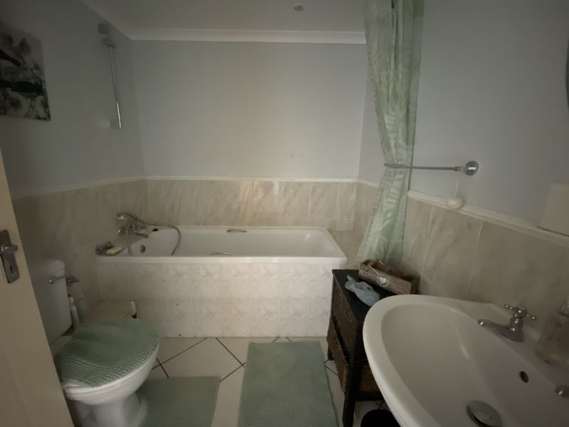 A functional bathroom featuring a bathtub with shower mixer, pedestal basin, and tiled finishes, offering a standard layout for an apartment.
