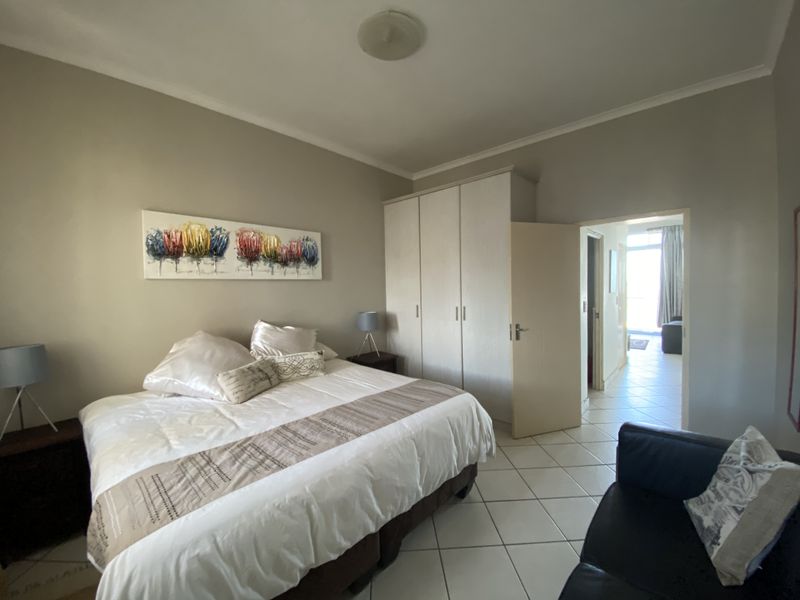A bedroom featuring built-in wardrobes, tiled flooring, and a neutral color palette, with an open doorway leading to an adjacent living area.