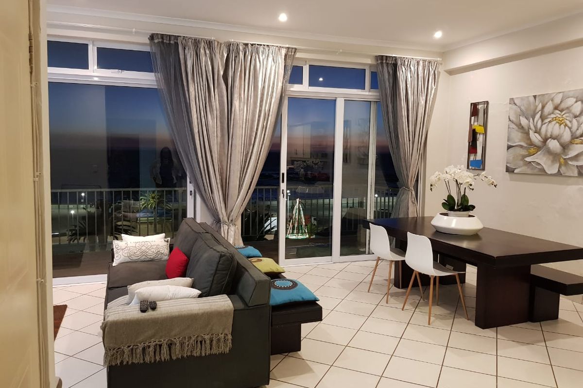 Spacious open-plan living and dining area featuring tiled floors, recessed lighting, and large sliding glass doors leading to a balcony with scenic views.