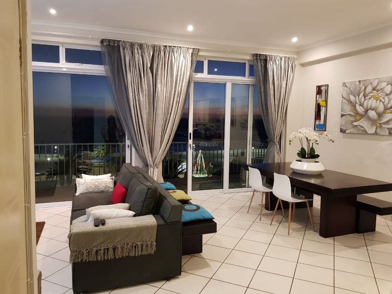 Spacious open-plan living and dining area featuring tiled floors, recessed lighting, and large sliding glass doors leading to a balcony with scenic views.