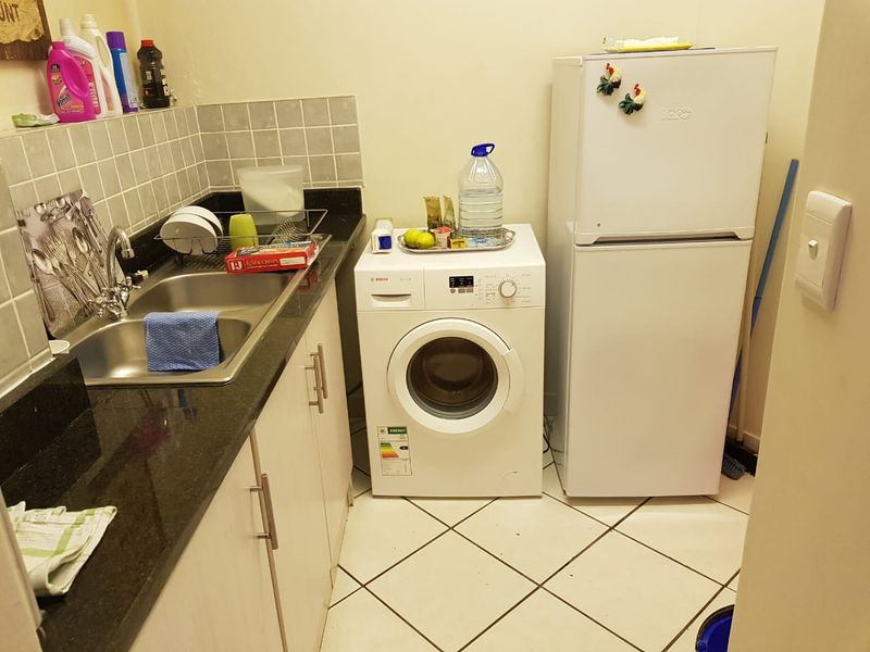 A functional laundry area featuring a stainless steel sink, granite countertops, tiled backsplash, and dedicated space for a washing machine and refrigerator.