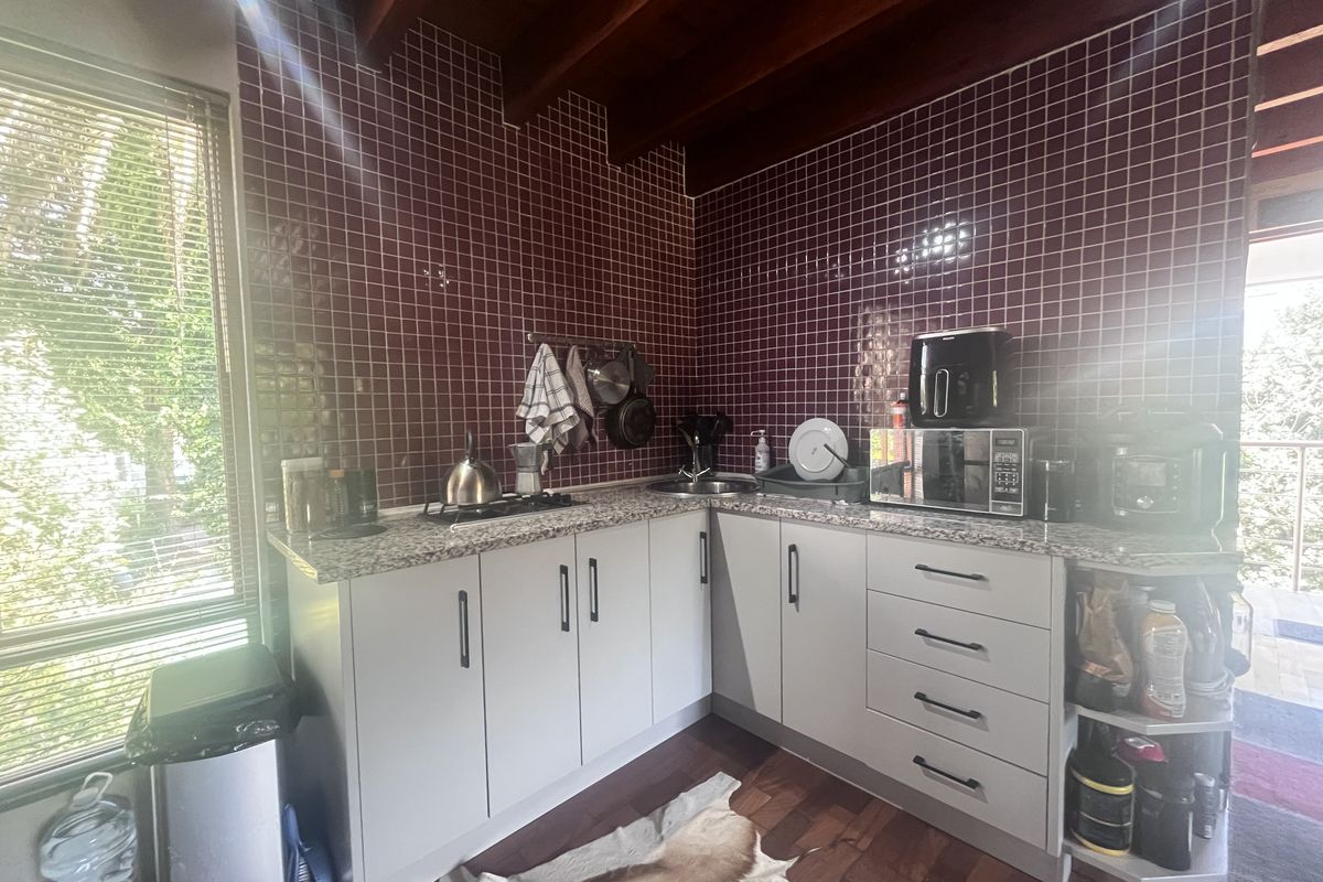 A functional kitchen featuring granite countertops, a tiled backsplash, and exposed timber ceiling beams, offering a practical layout with ample storage cabinetry.