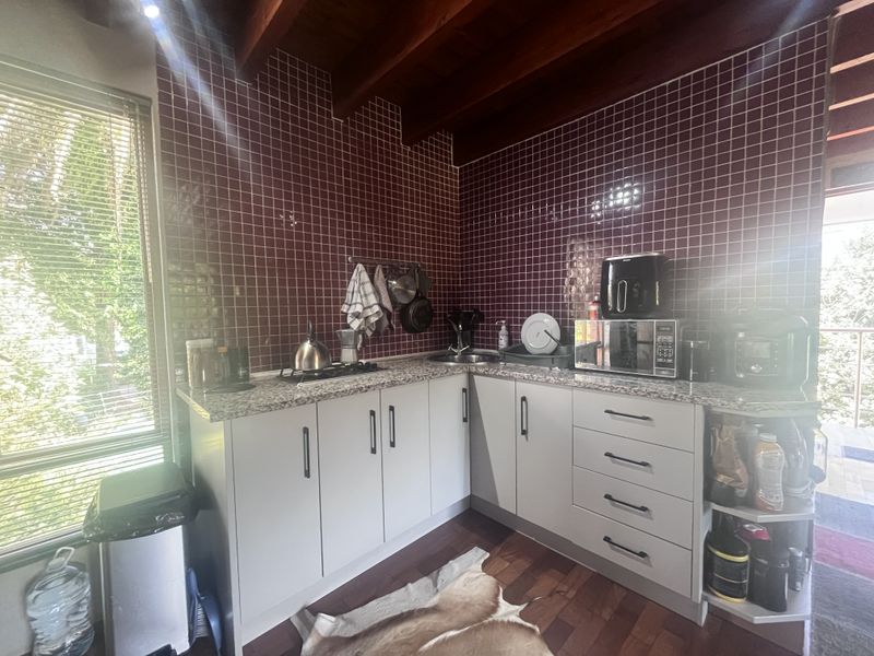 A functional kitchen featuring granite countertops, a tiled backsplash, and exposed timber ceiling beams, offering a practical layout with ample storage cabinetry.